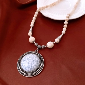 Detail view of round vintage silver pendant with white stone beads on red silk background