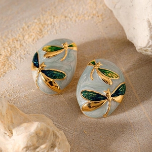 Detailed macro of oval gold dragonfly earrings with blue gradient enamel on stone background