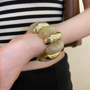 Close-up of chunky gold-toned metal bracelet with marble resin inserts on model