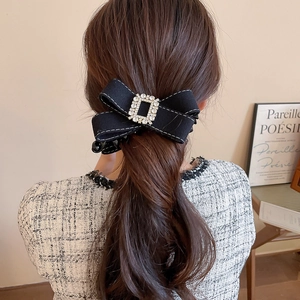 Detail of black bow hair clip with white stitching and rectangle crystal on a ponytail