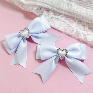Détail de deux barrettes à nœuds en satin bleu clair avec cœur en strass brillant