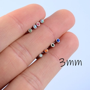 Detail shot of two 3mm opal labret studs in stainless steel held between fingers for scale