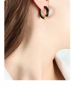 Close-up of modern black enamel hoop earrings with gold-toned accents worn by model