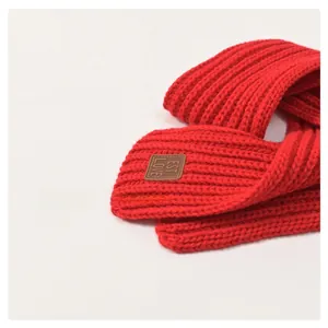 Detail of red ribbed knit kids scarf featuring a brown leather 'EST LOVE' label tag