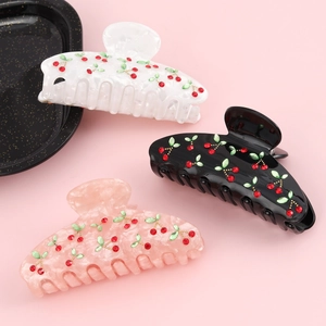 Three acetate hair claws with cherry rhinestone patterns on a soft pink background