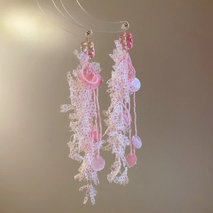 Detail of floral resin earrings with pink sequins, fabric tassels and gold metal hooks