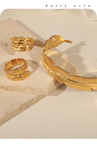 Detail of gold feather jewelry set featuring textured rings and open cuff on stone