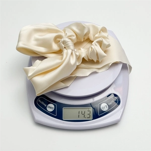 Detail showing the 14.3g weight of a beige satin bow hair scrunchie on a digital scale