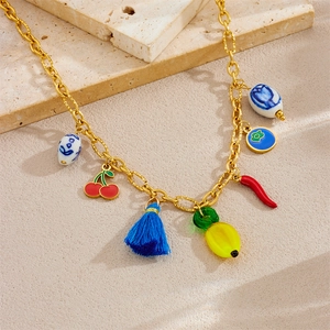 Golden chain necklace with colorful acrylic vegetable pendants and blue tassels on sand