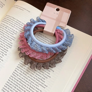 Détail de trois chouchous en dentelle élastique en bleu, rose et marron sur livre
