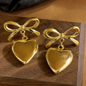 Close-up of golden metal bow and heart pendant earrings on a wooden background