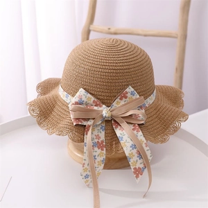 Detail of child straw hat featuring floral ribbon bow and wavy scalloped edge design