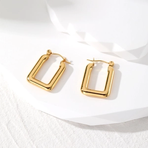 Detailed macro view of gold-finished geometric rectangular hoop earrings on white stone stand