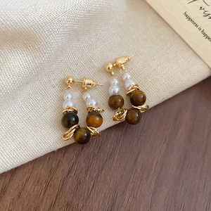 Detailed close-up of tiger eye and pearl earrings on a minimalist wooden and knit background