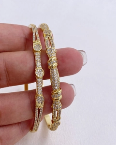 Dettaglio di bracciali aperti dorati con micro zirconi bianchi indossati su una mano