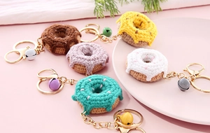 Detail of five colorful handmade crochet donut keychains with golden bells and hooks