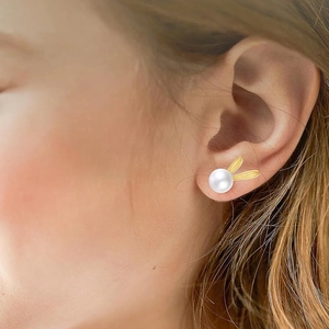 Close-up of golden bunny rabbit earrings with pearls worn by a model in a natural setting
