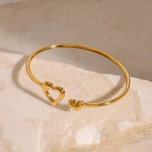 Detail of gold-plated heart-shaped bangle featuring one solid and one hollow heart charm