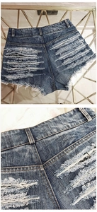 Detail of distressed high-waisted denim shorts with heavy ripped holes and fringe tassel hem