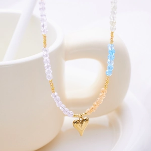 Bohemian multicolored beaded necklace with a golden heart pendant on a white porcelain cup