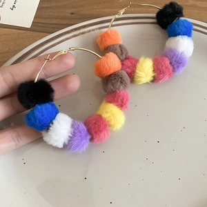 Detail of hand holding a large gold hoop earring with colorful dopamine fur balls