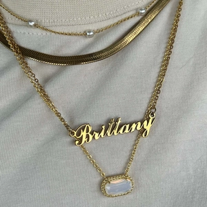 Layered 18K gold necklaces featuring a Brittany letter charm and oval white gemstone
