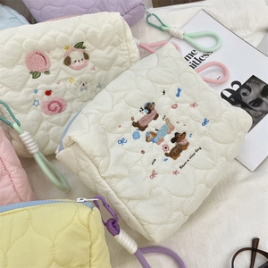 Close-up of quilted cream makeup bag with heart embroidery and colorful zipper strap