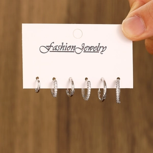 Close-up of six-piece silver earring set with crystals on display card over wood background
