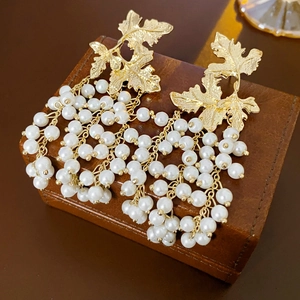 Vintage-Ohrringe mit goldenem Ahornblatt und eleganten weißen Perlen-Quasten auf Holz