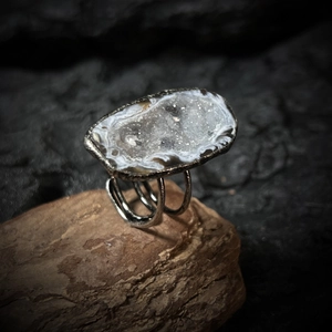 Macro shot of silver adjustable ring featuring raw natural geode crystal on wood base