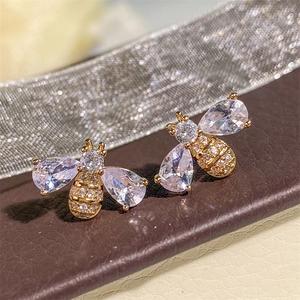 Detailed macro view of bee-shaped stud earrings with micro-set zircons on brown leather