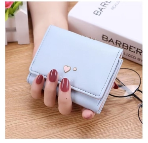 Close-up of light blue trifold wallet with pink heart metal detail held over a wooden desk