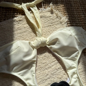 Detail of cream-colored halter bikini top featuring a central twist knot and smooth fabric