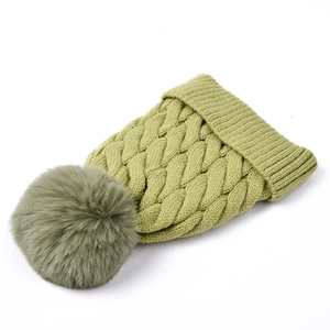 Detail of chunky cable knit grass green winter hat with fluffy faux fur pom-pom topper