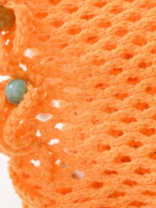 Macro detail of orange hand-knitted fabric texture with green decorative beads