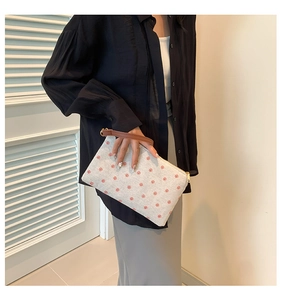 Detail of off-white canvas clutch bag with red floral print and brown leather wristlet