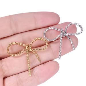 Close-up of gold and silver stainless steel bow pendants held in a hand for size detail