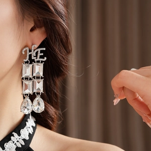 Close-up of silver long earrings with HE initials and sparkling square crystal drops