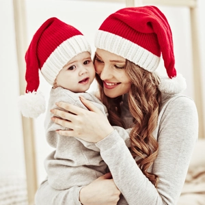 Close-up of mother and baby wearing red knitted Christmas hats with white pom-poms