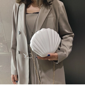 Detail of white shell-shaped evening bag with glossy finish and gold chain strap