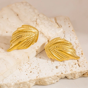 Macro shot of gold feather earrings with detailed texture on a textured stone background