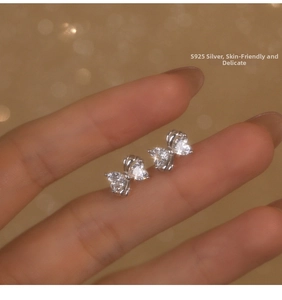 Detailed view of S925 sterling silver bow earrings with sparkling cubic zirconia held by hand