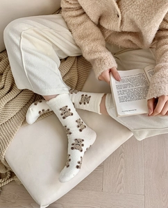 Close-up of white coral fleece socks with brown bear pattern in a cozy home setting