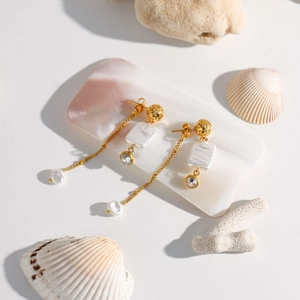 Elegant gold bow earrings with pearls and mother-of-pearl shell on beach decor