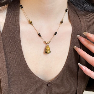 Macro view of gold necklace with brown gourd pendant and beaded chain on a model