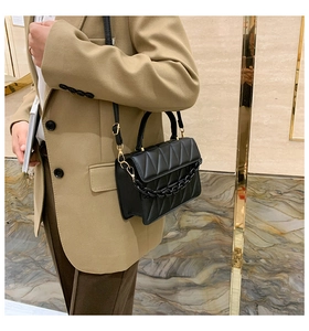 Vue latérale d'un sac à bandoulière matelassé noir porté par un mannequin en tailleur