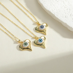 Three golden heart evil eye necklaces in green and blue enamel on textured background