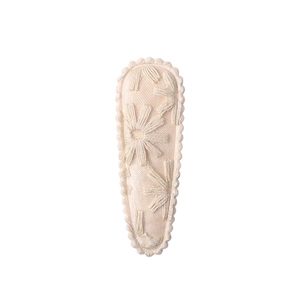 Close-up of beige floral embroidery on fabric teardrop hair clip with scalloped edges