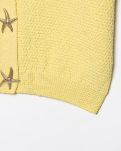 Détail de maille gaufrée jaune avec boutons étoiles de mer dorés et bordure côtelée