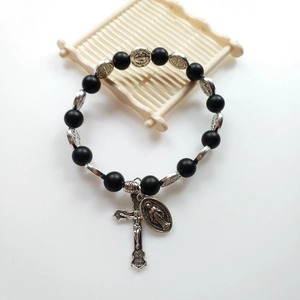 Macro detail of a black beaded rosary bracelet with silver crucifix and medal pendant
